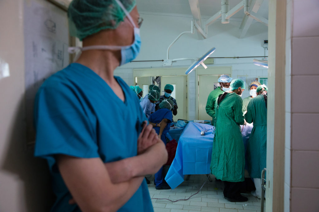 Doctor gazes at doctors performing surgery in the background